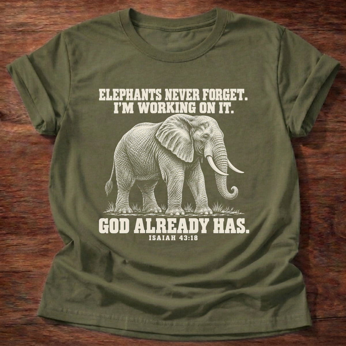 Military Green t-shirt printed with an elephant walking through tall grass graphic and 'Elephants never forget. I'm working on it. God already has.' Isaiah 43:18 faith based gift