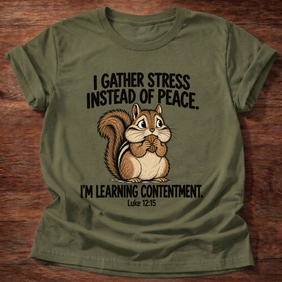 Military Green t-shirt printed with a squirrel gathering acorns graphic and 'I gather stress instead of peace. I'm learning contentment.' Luke 12:15 faith based gift