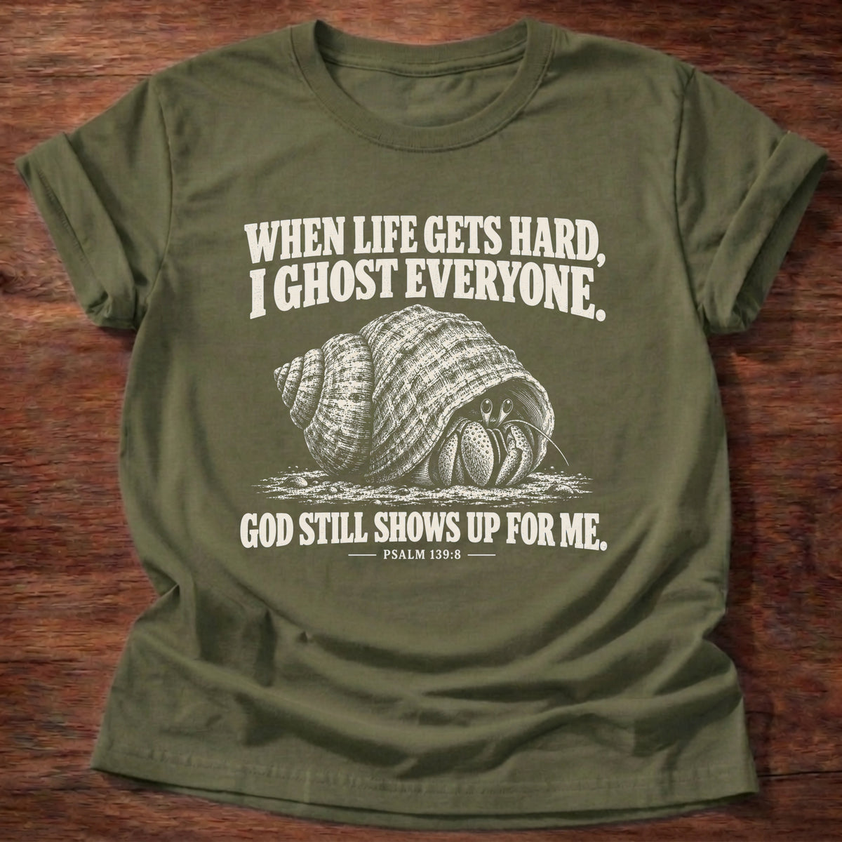 Military Green t-shirt printed with a hermit crab retreating into its shell graphic and 'When life gets hard, I ghost everyone. God still shows up for me.' Psalm 139:8 faith based gift