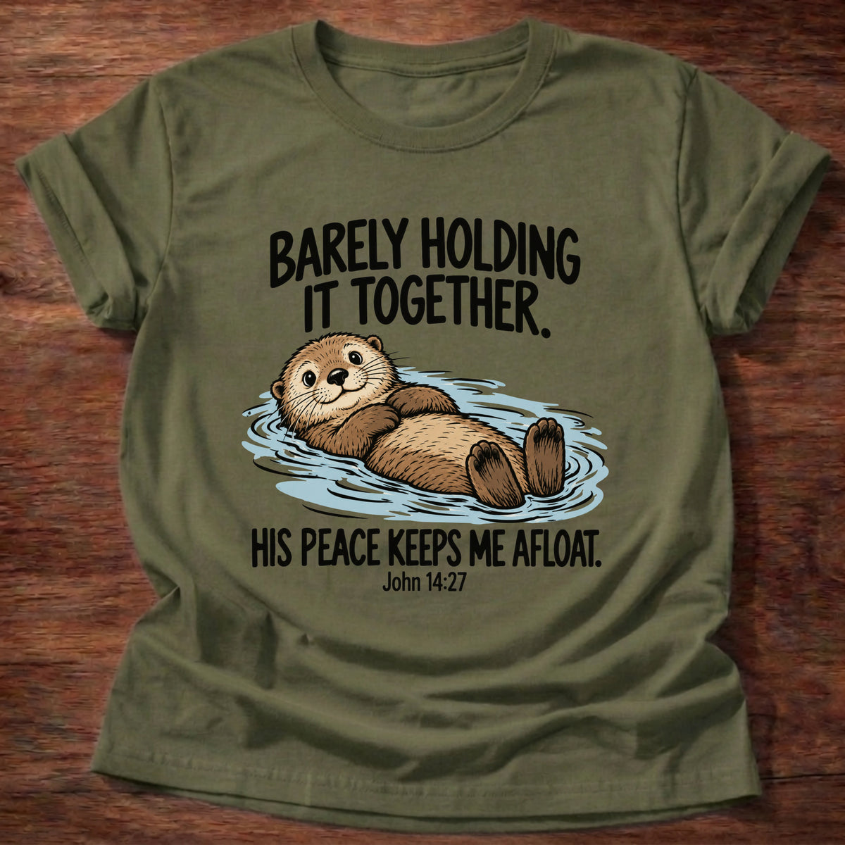 Military Green t-shirt printed with an otter floating on its back graphic and 'Barely holding it together. His peace keeps me afloat.' John 14:27 faith based gift