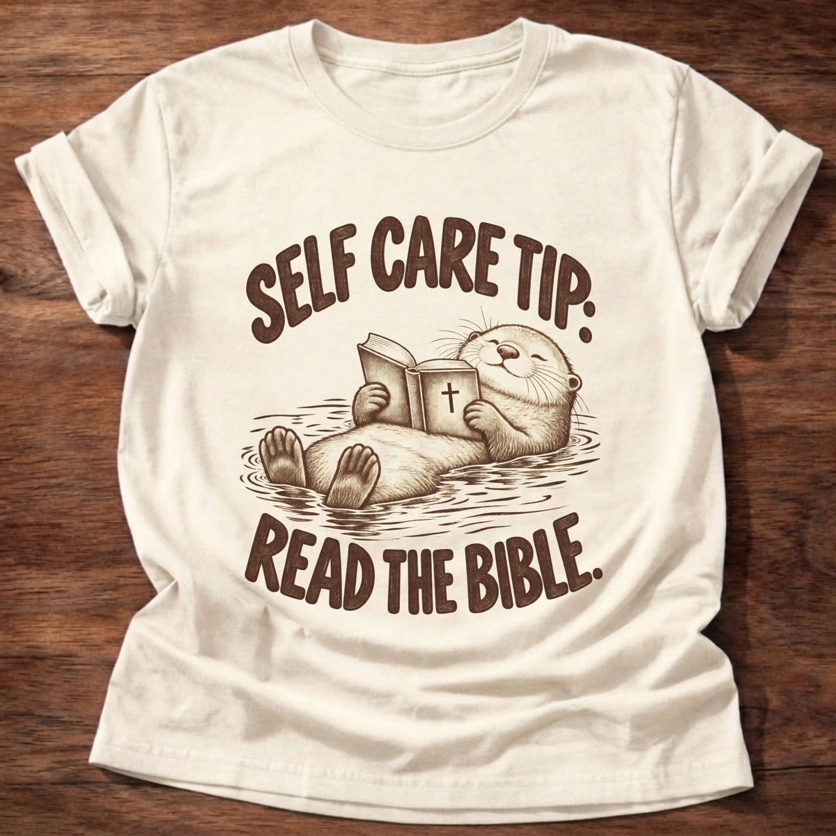 Natural t-shirt printed with a sea otter floating on its back reading a Bible graphic and “Self care tip: Read the Bible.” faith based gift