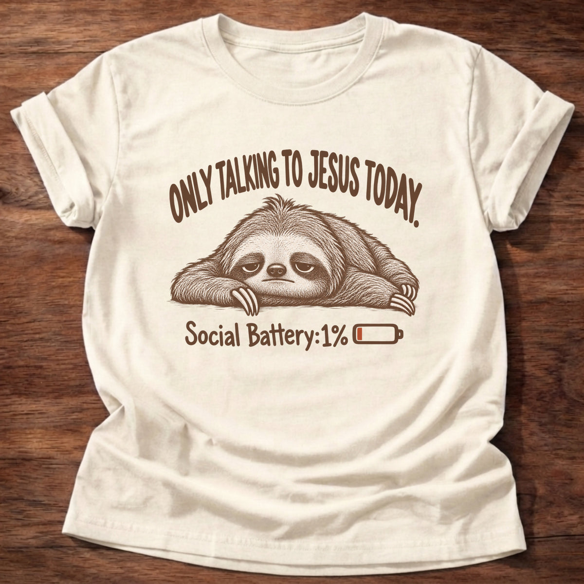 Natural t-shirt printed with an exhausted sloth lying flat next to a nearly empty battery icon graphic and “Only talking to Jesus today. Social Battery: 1%” faith based gift