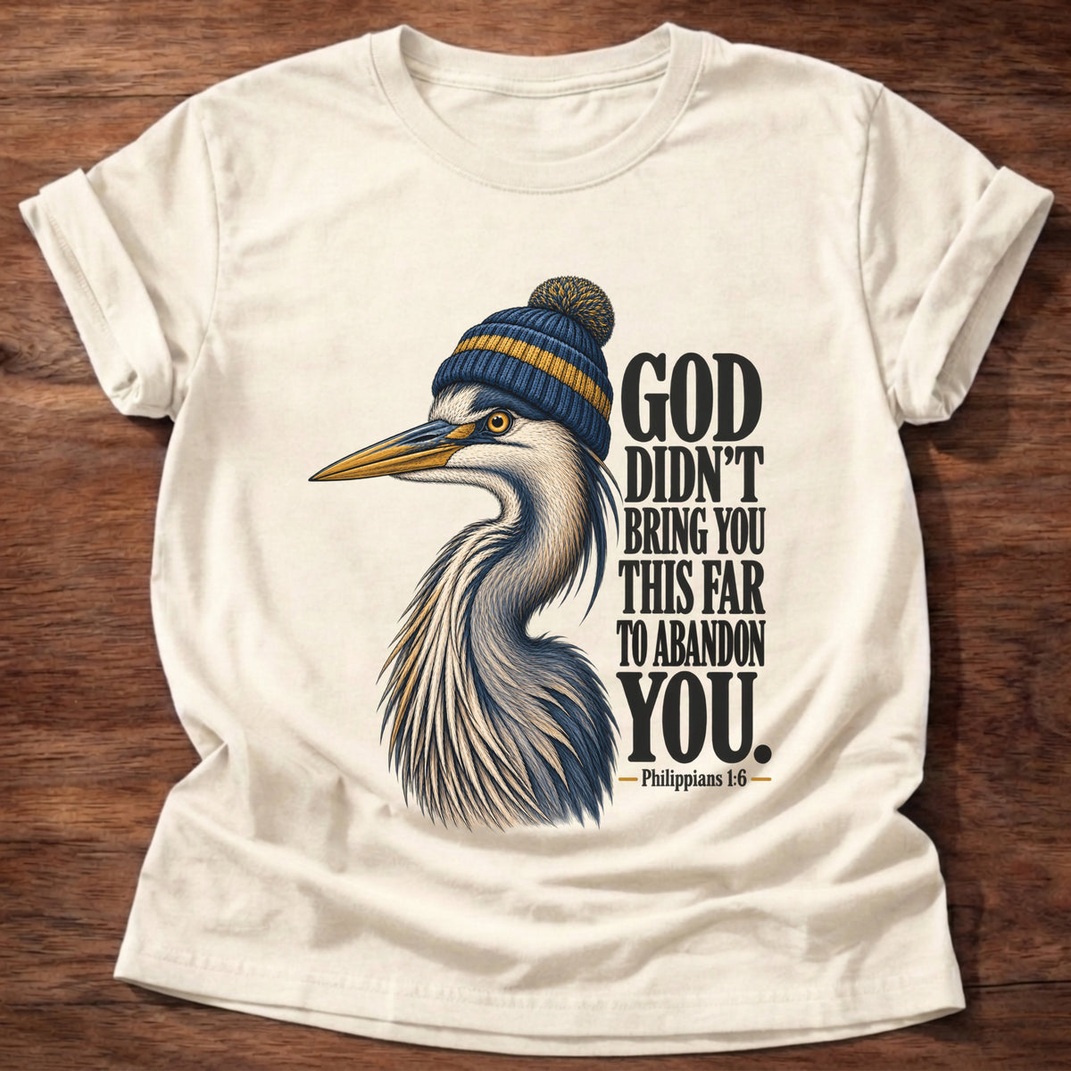Natural t-shirt printed with a great blue heron wearing a knit beanie graphic and “God didn't bring you this far to abandon you.” Philippians 1:6 faith based gift