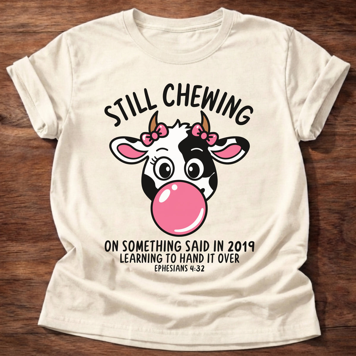 Natural t-shirt printed with a cow blowing a bubblegum bubble and “Still chewing on something said in 2019. Learning to hand it over.” Ephesians 4:32 Christian shirt