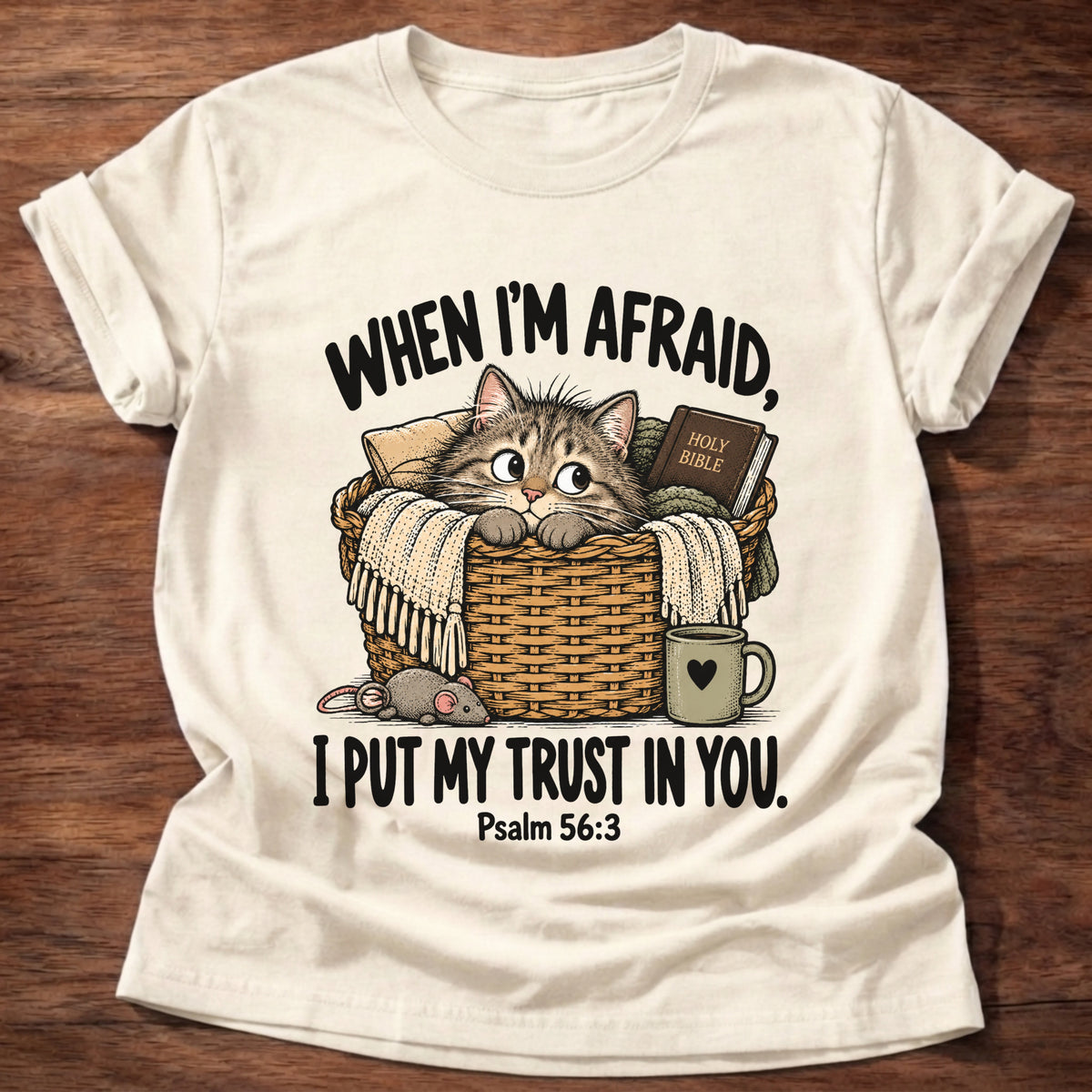 Natural t-shirt printed with a wide-eyed kitten peeking out of a wicker basket beside a Holy Bible, a heart mug and a toy mouse graphic and “When I'm afraid, I put my trust in You.” Psalm 56:3 faith based gift