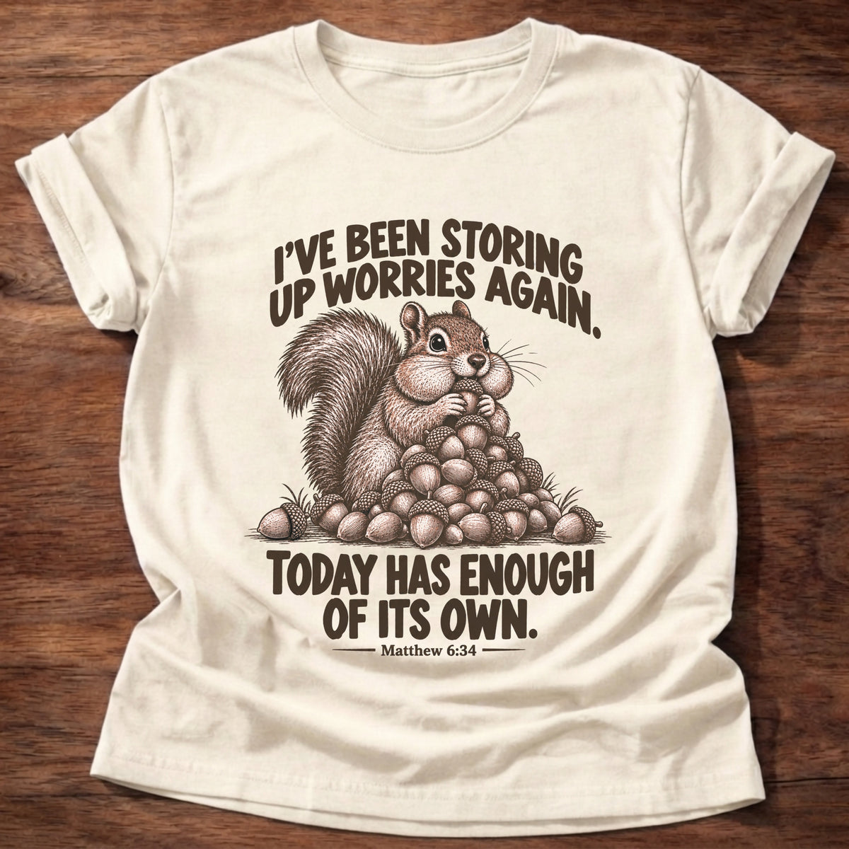 Natural t-shirt printed with a squirrel sitting on a big pile of acorns graphic and “I've been storing up worries again. Today has enough of its own.” Matthew 6:34 faith based gift