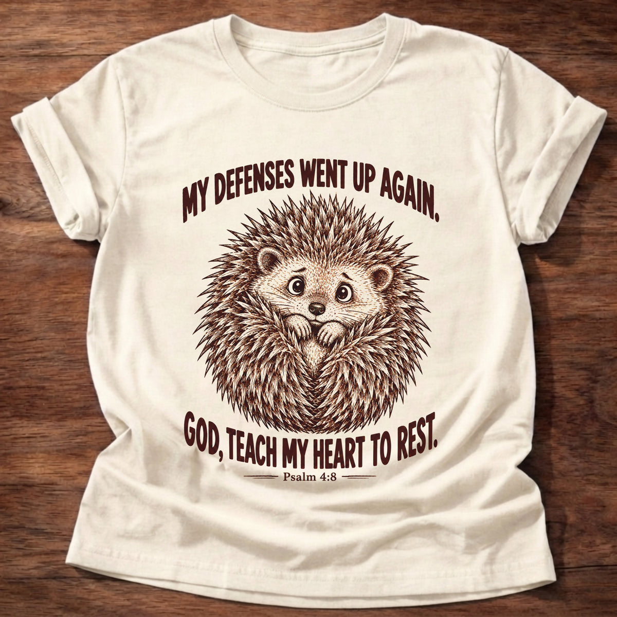 Natural t-shirt printed with a worried hedgehog curled up with its quills raised graphic and “My defenses went up again. God, teach my heart to rest.” Psalm 4:8 faith based gift