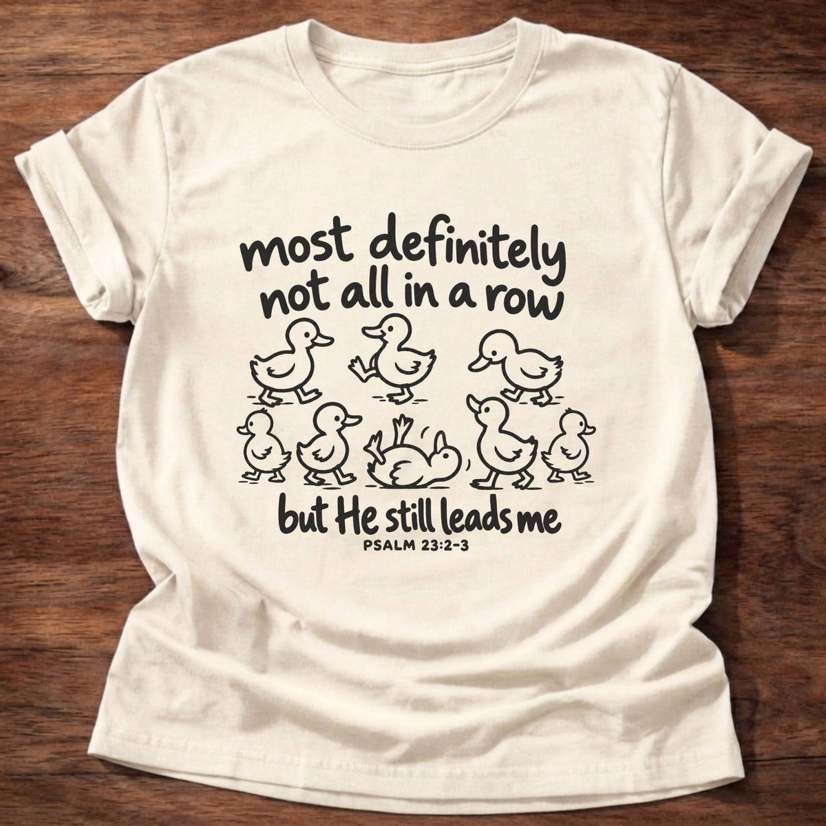 Natural t-shirt printed with a scattered line of hand-drawn ducklings graphic and “Most definitely not all in a row, but He still leads me.” Psalm 23:2-3 Christian shirt