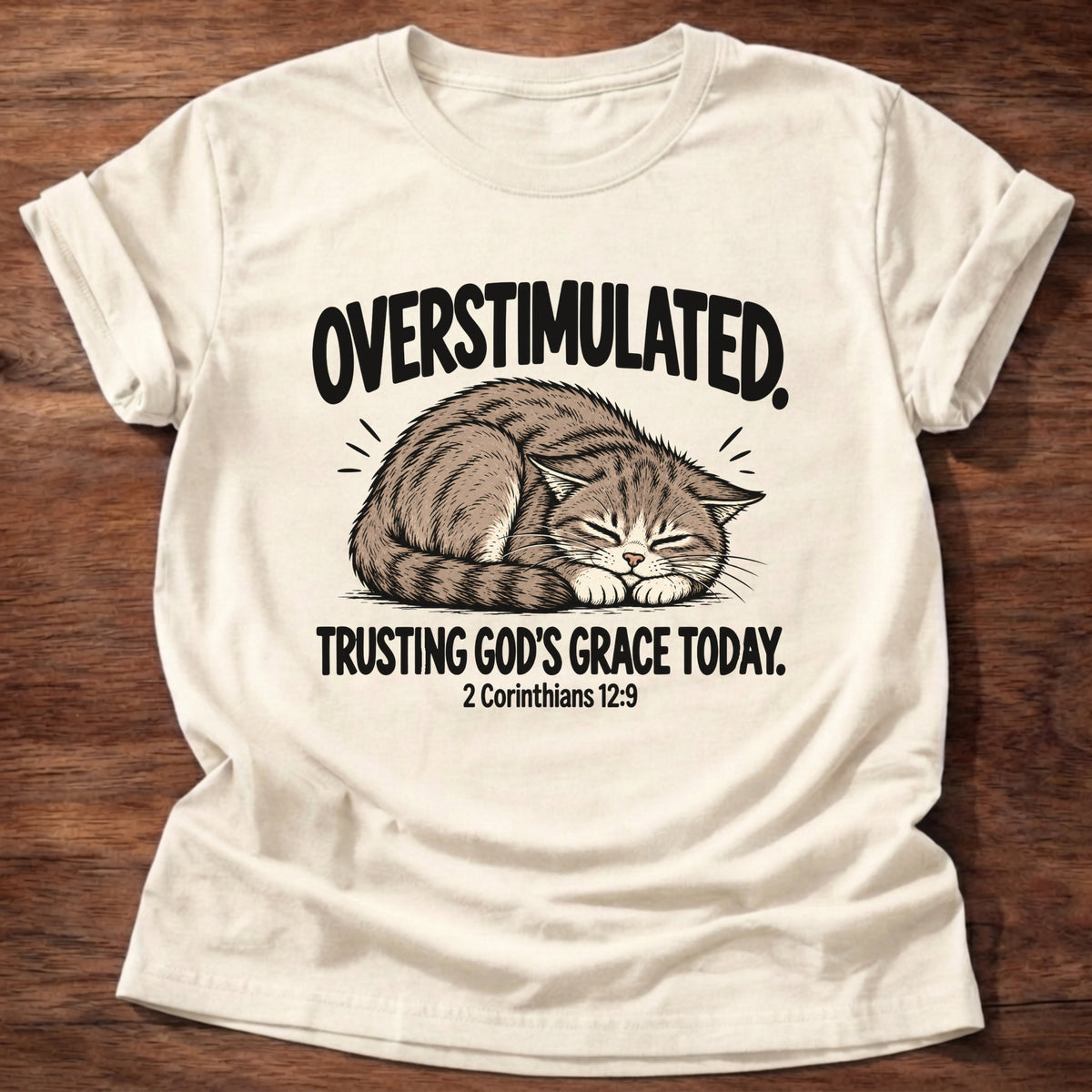 Natural t-shirt printed with a cat curled asleep graphic and 'Overstimulated. Trusting God's grace today.' 2 Corinthians 12:9 faith based gift