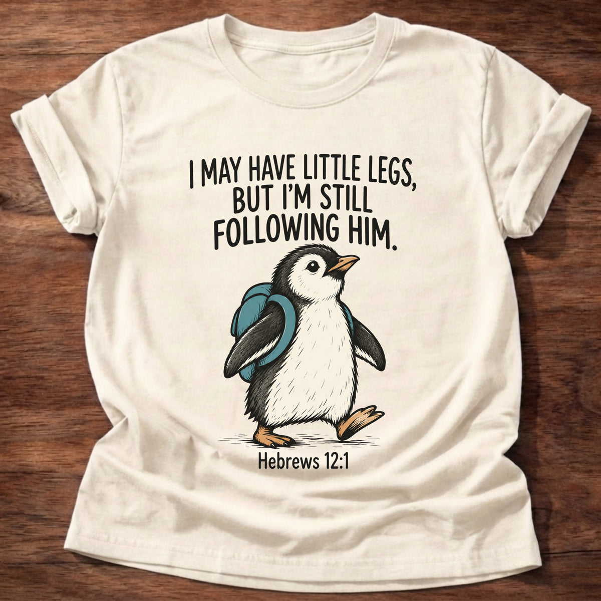 Natural t-shirt printed with a penguin graphic and 'I may have little legs, but I'm still following Him.' Hebrews 12:1 faith based gift