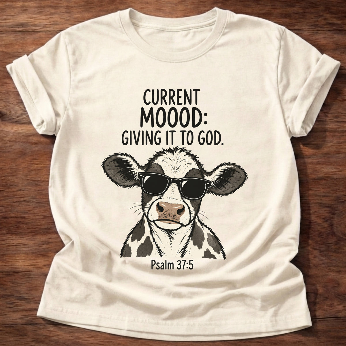 Natural t-shirt printed with a sunglasses-wearing cow graphic and 'Current moood: giving it to God.' Psalm 55:22 faith based gift
