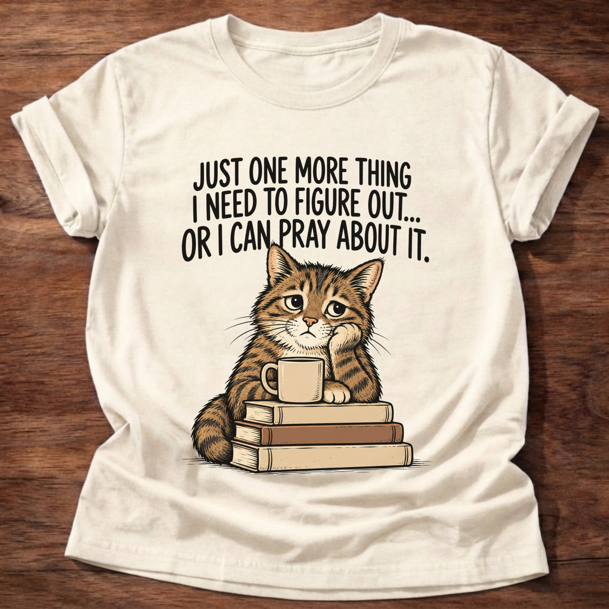 Natural t-shirt printed with a cat surrounded by books graphic and 'Just one more thing I need to figure out... or I can pray about it.' Philippians 4:6-7 faith based gift