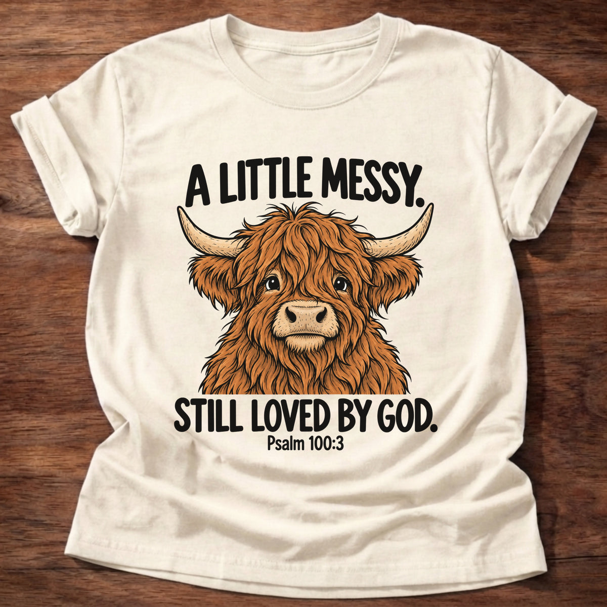Natural t-shirt printed with a highland cow graphic and 'A little messy. Still loved by God.' Psalm 100:3 faith based gift
