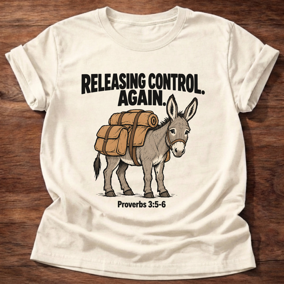 Natural t-shirt printed with a donkey carrying a backpack graphic and 'Releasing control. Again.' Proverbs 3:5-6 faith based gift