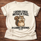 Natural t-shirt printed with a squirrel gathering acorns graphic and 'I gather stress instead of peace. I'm learning contentment.' Luke 12:15 faith based gift
