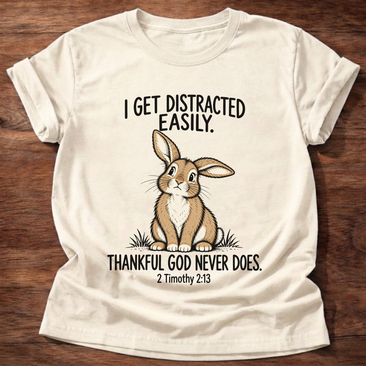 Natural t-shirt printed with a rabbit graphic and 'I get distracted easily. Thankful God never does.' 2 Timothy 2:13 faith based gift