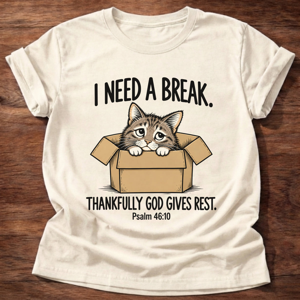 Natural t-shirt printed with a cat curled in a cardboard box graphic and 'I need a break. Thankfully God gives rest.' Psalm 46:10 faith based gift