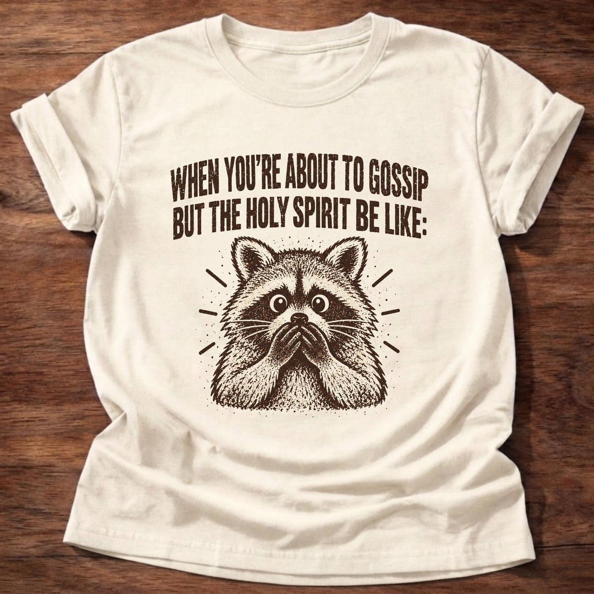 Natural t-shirt printed with a startled raccoon graphic and 'When you're about to gossip but the Holy Spirit be like.' Proverbs 16:28 faith based gift