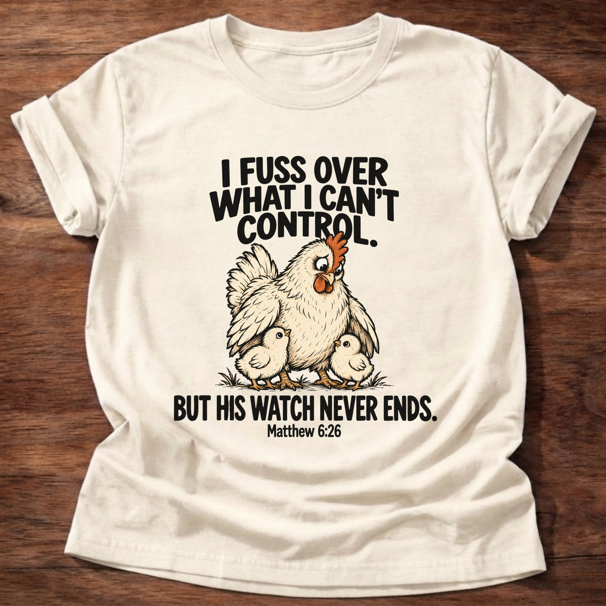 Natural t-shirt printed with a fussing hen graphic and 'I fuss over what I can't control. But His watch never ends.' Matthew 6:26 faith based gift