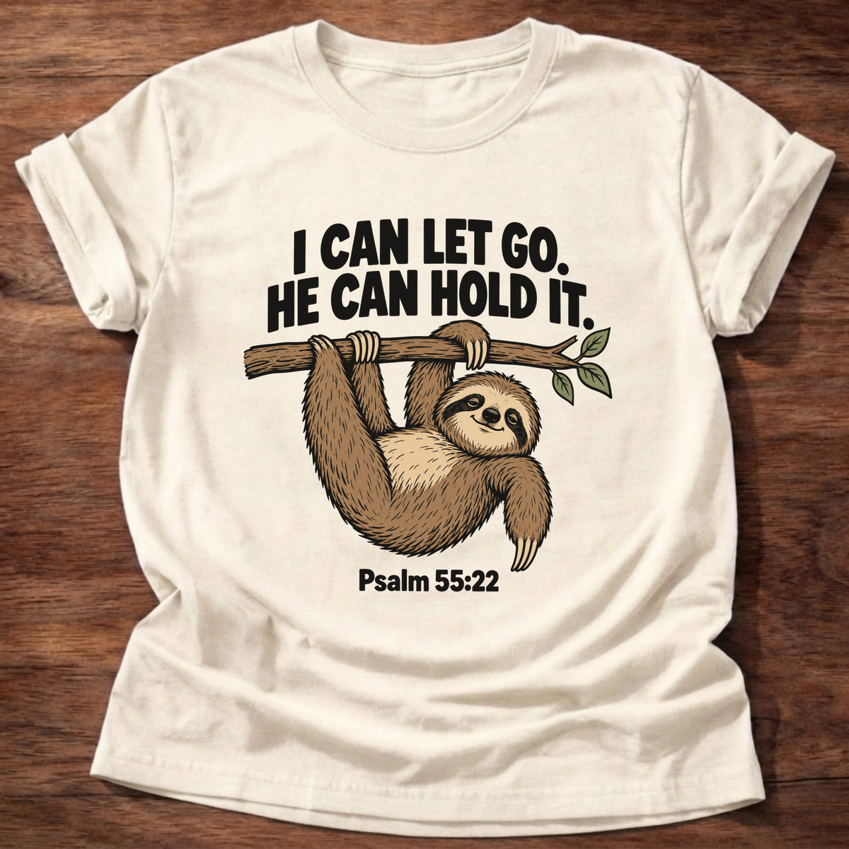 Natural t-shirt printed with a sloth hanging from a branch graphic and 'I can let go. He can hold it.' Psalm 55:22 faith based gift