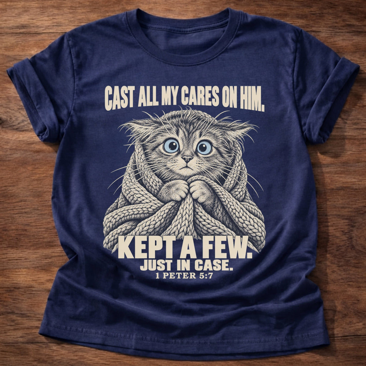 Kept A Few T-Shirt in Navy featuring a wide-eyed cat wrapped in a knit blanket and 1 Peter 5:7 anxiety humor design