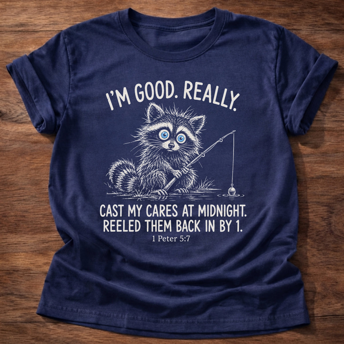 Navy t-shirt printed with a raccoon holding a fishing rod graphic and “I'm good. Really. Cast my cares at midnight. Reeled them back in by 1.” 1 Peter 5:7 Christian shirt