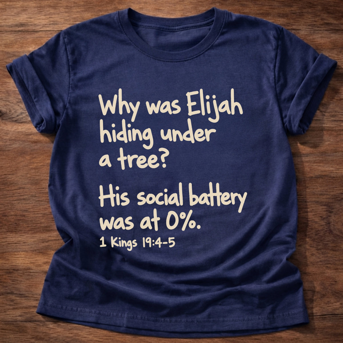 Navy t-shirt printed with a simple hand-lettered Bible joke graphic and “Why was Elijah hiding under a tree? His social battery was at 0%.” 1 Kings 19:4-5 Christian shirt