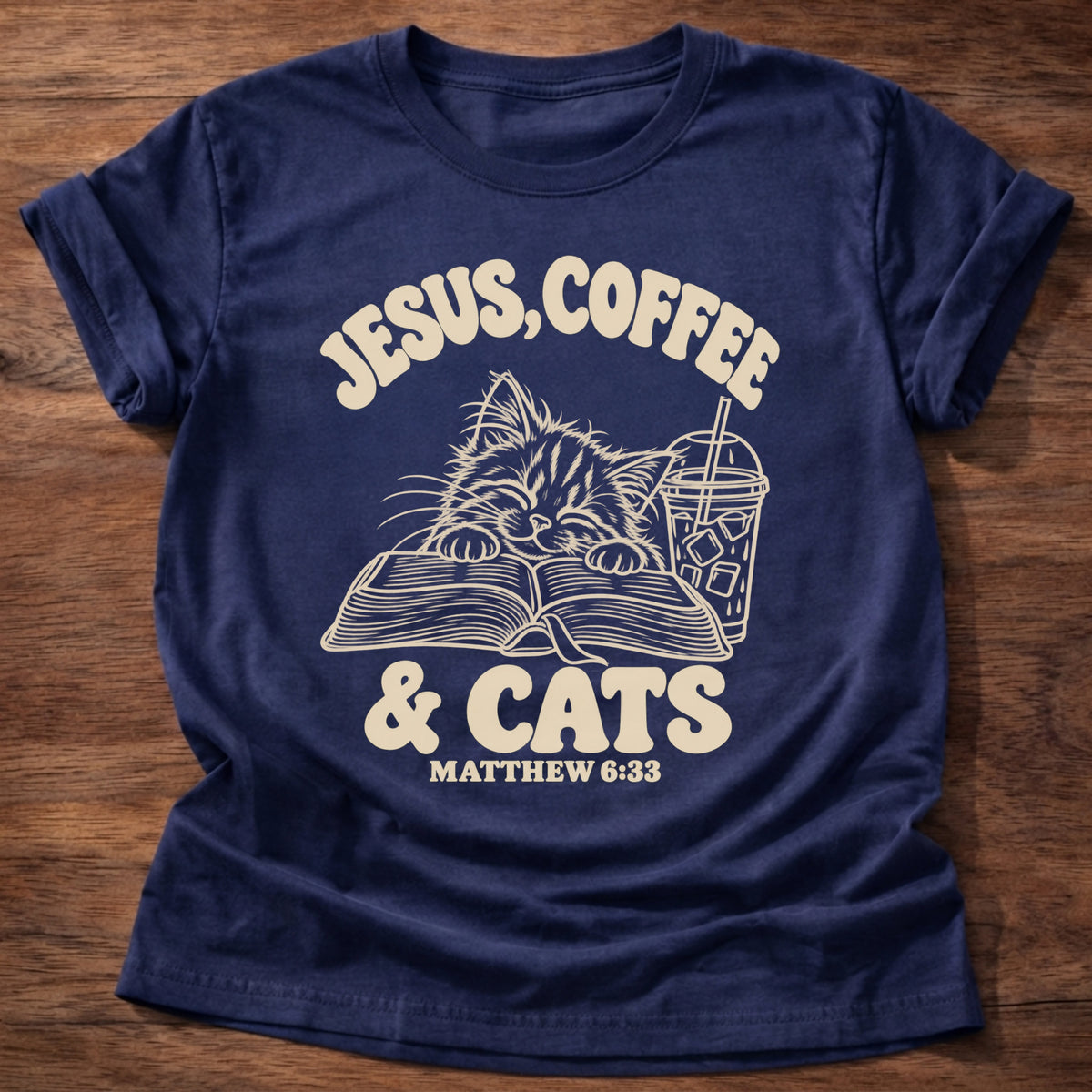 Navy t-shirt printed with a kitten reading an open Bible beside an iced coffee and “Jesus, Coffee & Cats” Matthew 6:33 Christian shirt
