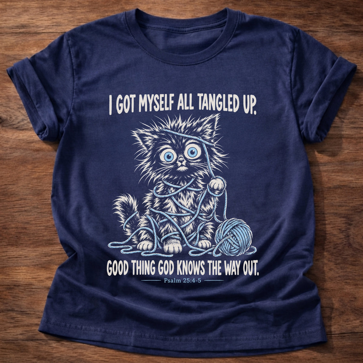 Navy t-shirt printed with a wide-eyed kitten tangled up in blue yarn next to a yarn ball graphic and “I got myself all tangled up. Good thing God knows the way out.” Psalm 25:4-5 faith based gift