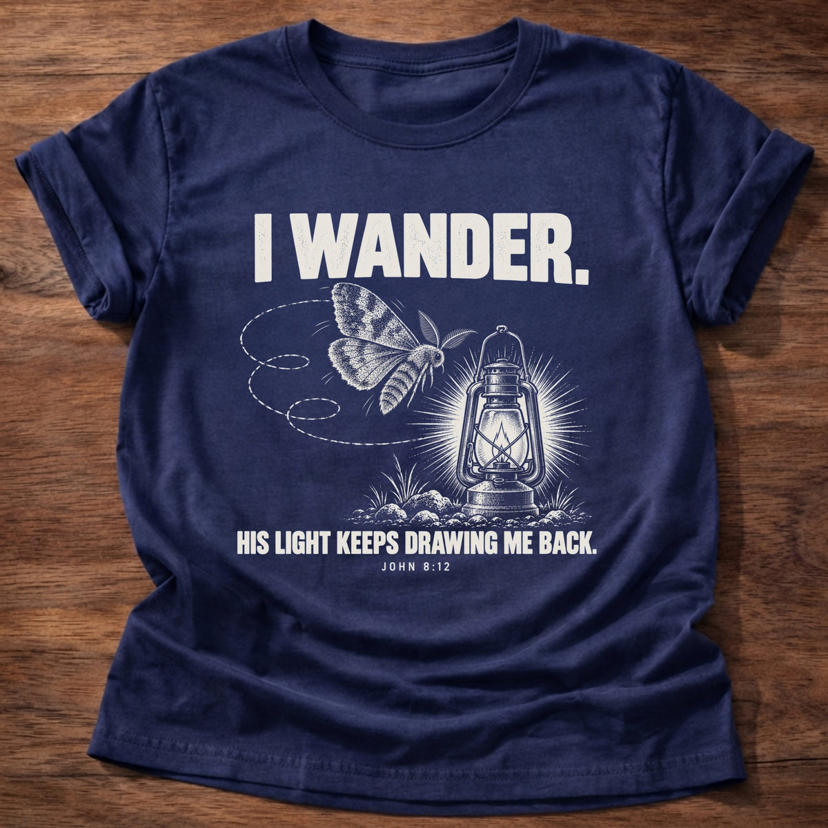 Navy t-shirt printed with a moth circling a glowing lantern graphic and 'I wander. His light keeps drawing me back.' John 8:12 faith based gift