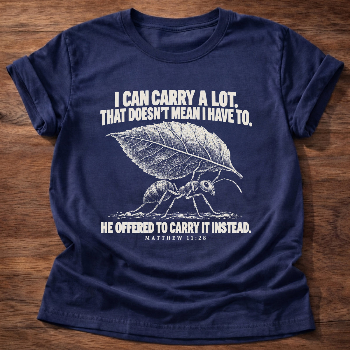 Navy t-shirt printed with an ant hauling a leaf many times its size graphic and 'I can carry a lot. That doesn't mean I have to. He offered to carry it instead.' Matthew 11:28 faith based gift