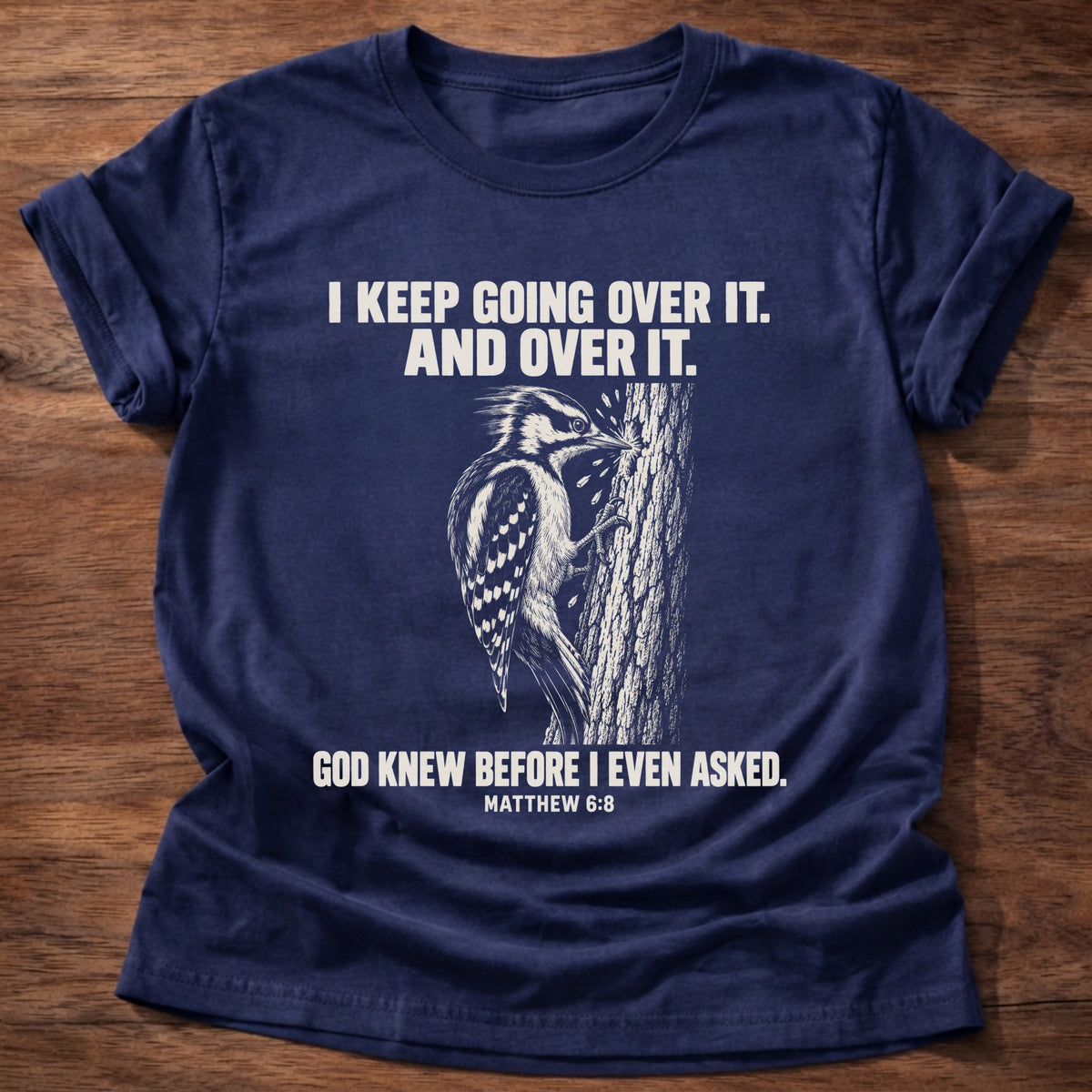Navy t-shirt printed with a woodpecker drumming the same spot on a tree graphic and 'I keep going over it. And over it. God knew before I even asked.' Matthew 6:8 faith based gift