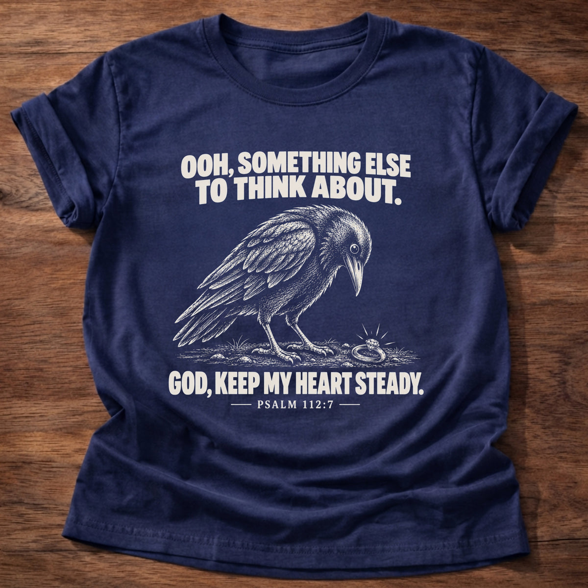 Navy t-shirt printed with a crow investigating something shiny on the ground graphic and 'Ooh, something else to think about. God, keep my heart steady.' Psalm 112:7 faith based gift