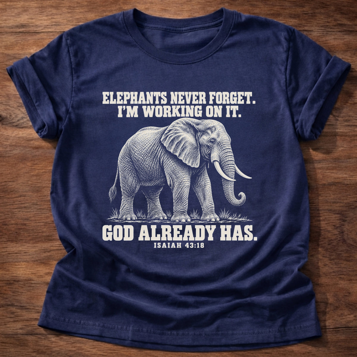 Navy t-shirt printed with an elephant walking through tall grass graphic and 'Elephants never forget. I'm working on it. God already has.' Isaiah 43:18 faith based gift