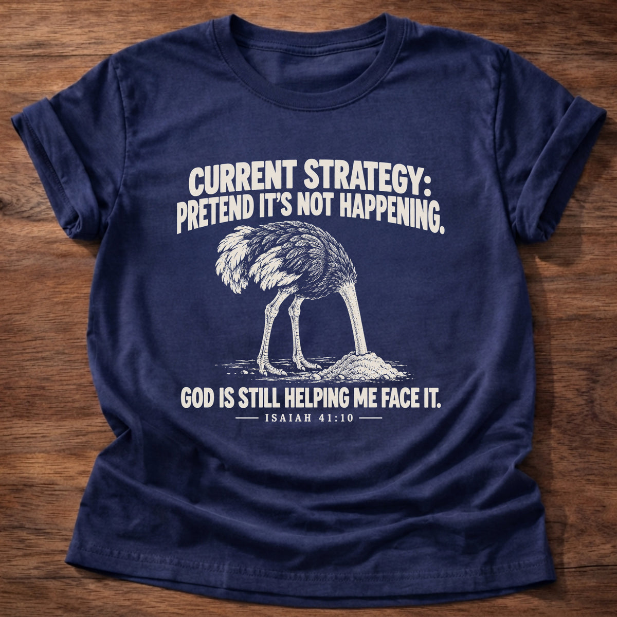 Navy t-shirt printed with an ostrich with its head buried in the sand graphic and 'Current strategy: pretend it's not happening. God is still helping me face it.' Isaiah 41:10 faith based gift