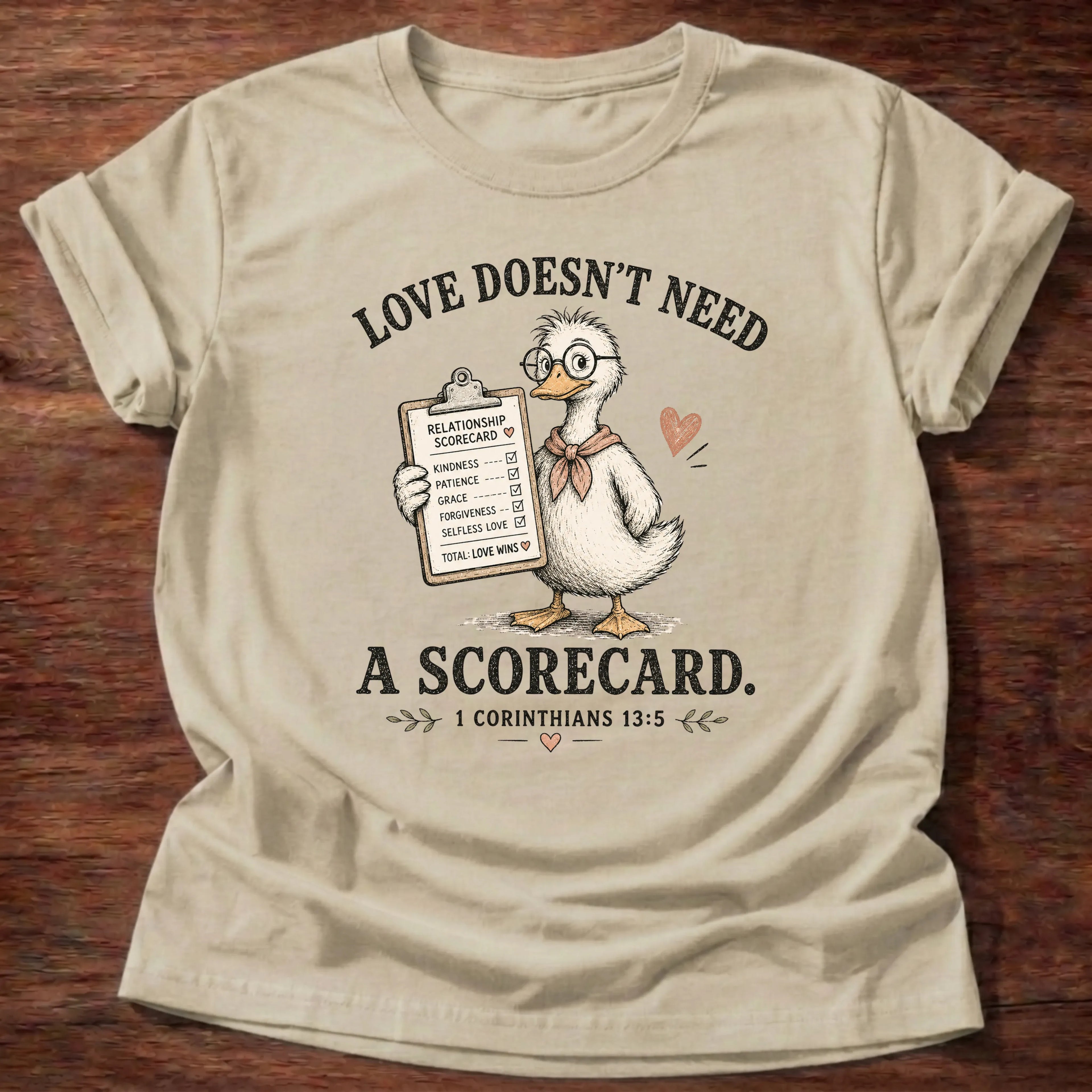 Sand Gildan 64000 t-shirt with a duck wearing glasses illustration and 'Love Doesn't Need A Scorecard' text, 1 Corinthians 13:5 Christian t-shirt