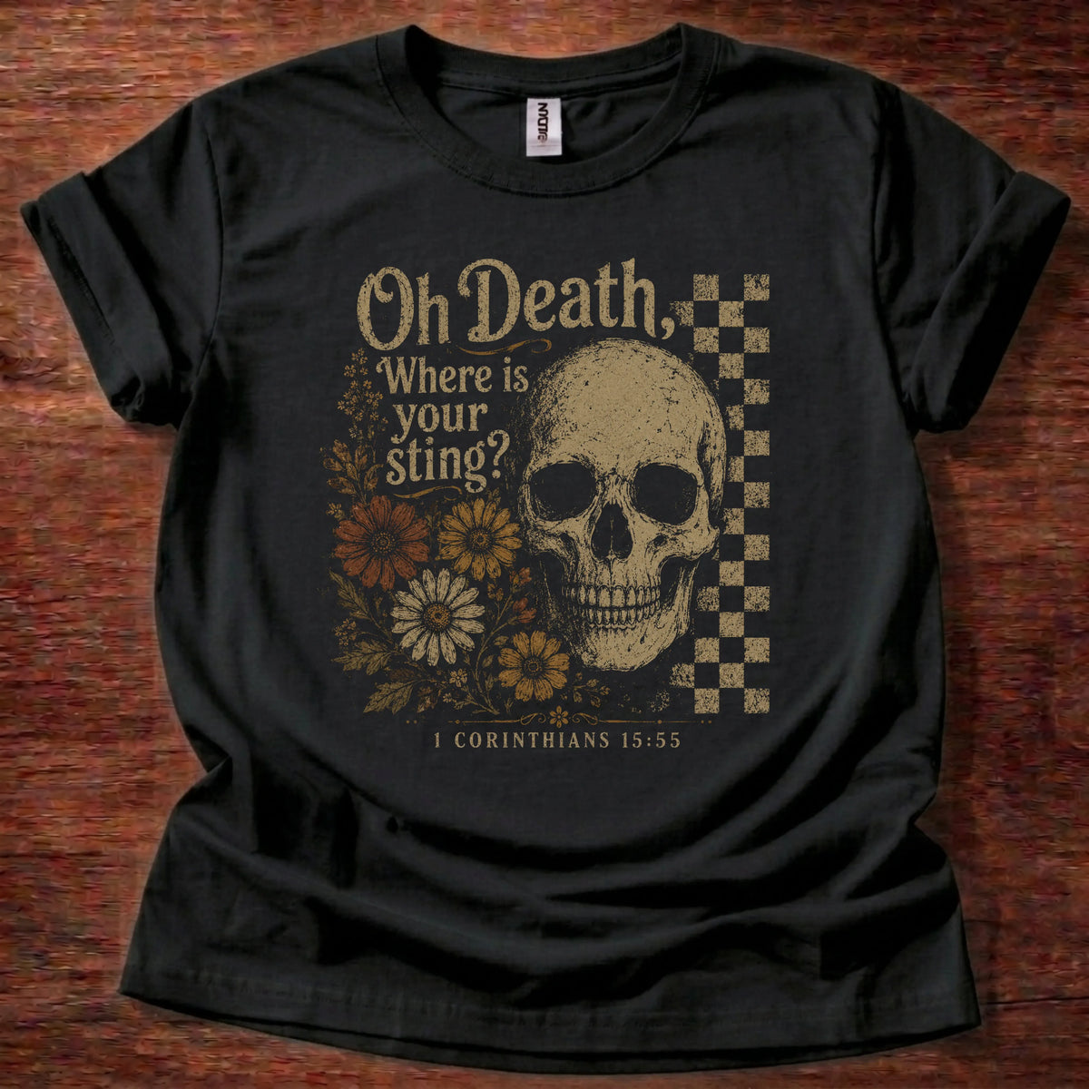 Black t-shirt with a large gold skull, checkerboard accent panel, and a floral cluster beneath text reading Oh Death, Where Is Your Sting, 1 Corinthians 15:55