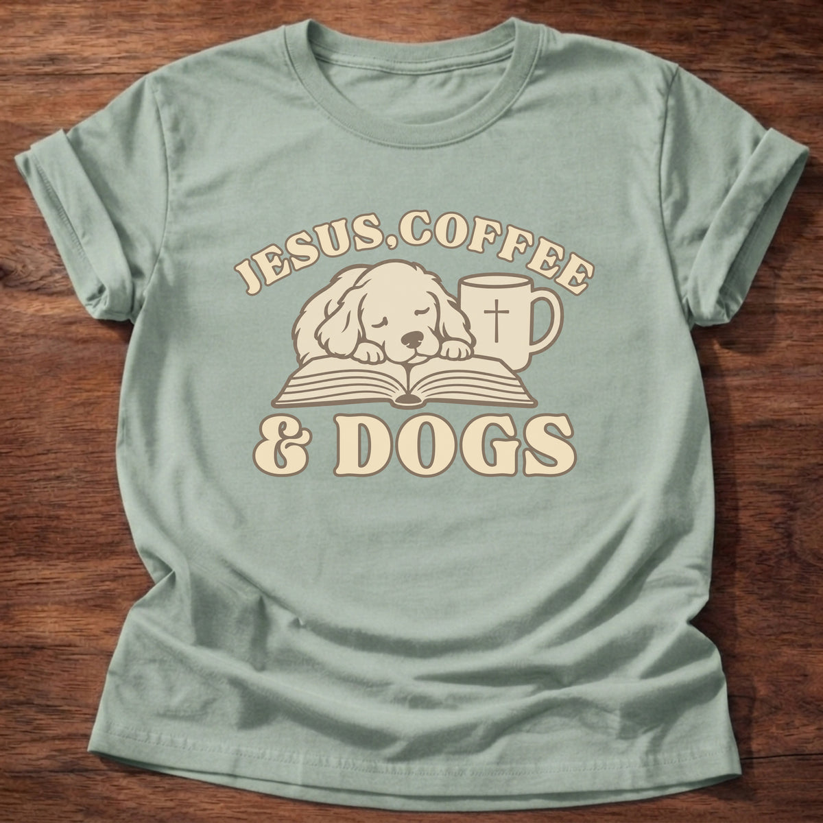 Sage t-shirt printed with a sleepy puppy resting on an open Bible beside a coffee mug with a cross and “Jesus, Coffee & Dogs” Christian shirt