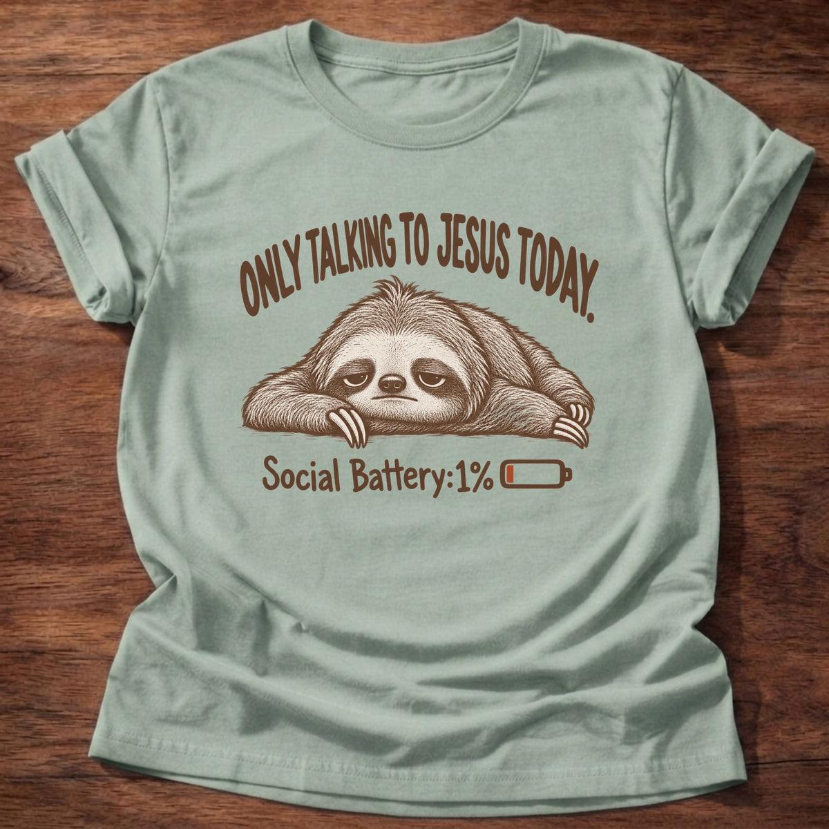 Sage t-shirt printed with an exhausted sloth lying flat next to a nearly empty battery icon graphic and “Only talking to Jesus today. Social Battery: 1%” faith based gift