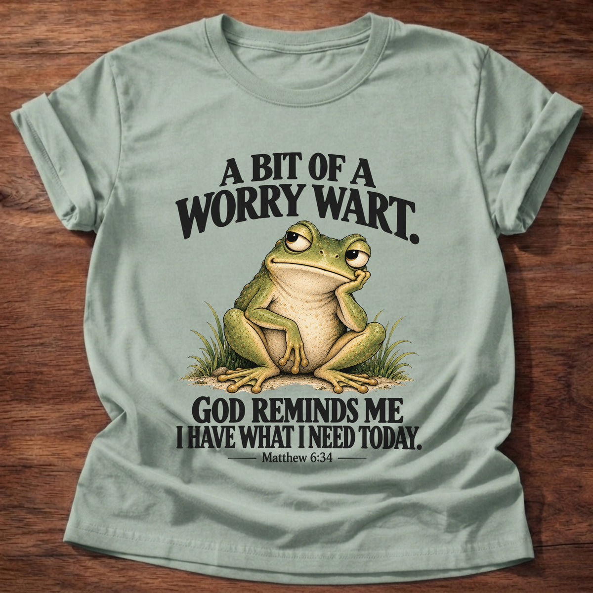 Sage t-shirt printed with a pensive frog resting its chin on its hand graphic and “A bit of a worry wart. God reminds me I have what I need today.” Matthew 6:34 faith based gift