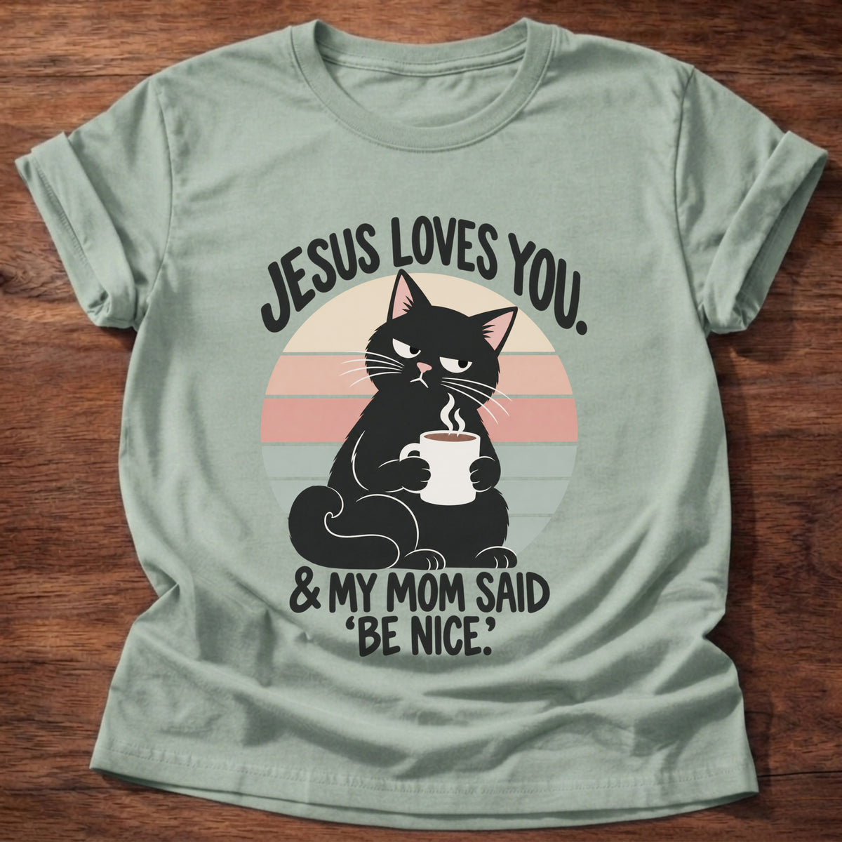 Sage t-shirt printed with a grumpy black cat holding a steaming coffee mug in front of a retro striped sunset graphic and “Jesus loves you. & my mom said 'be nice.'” faith based gift