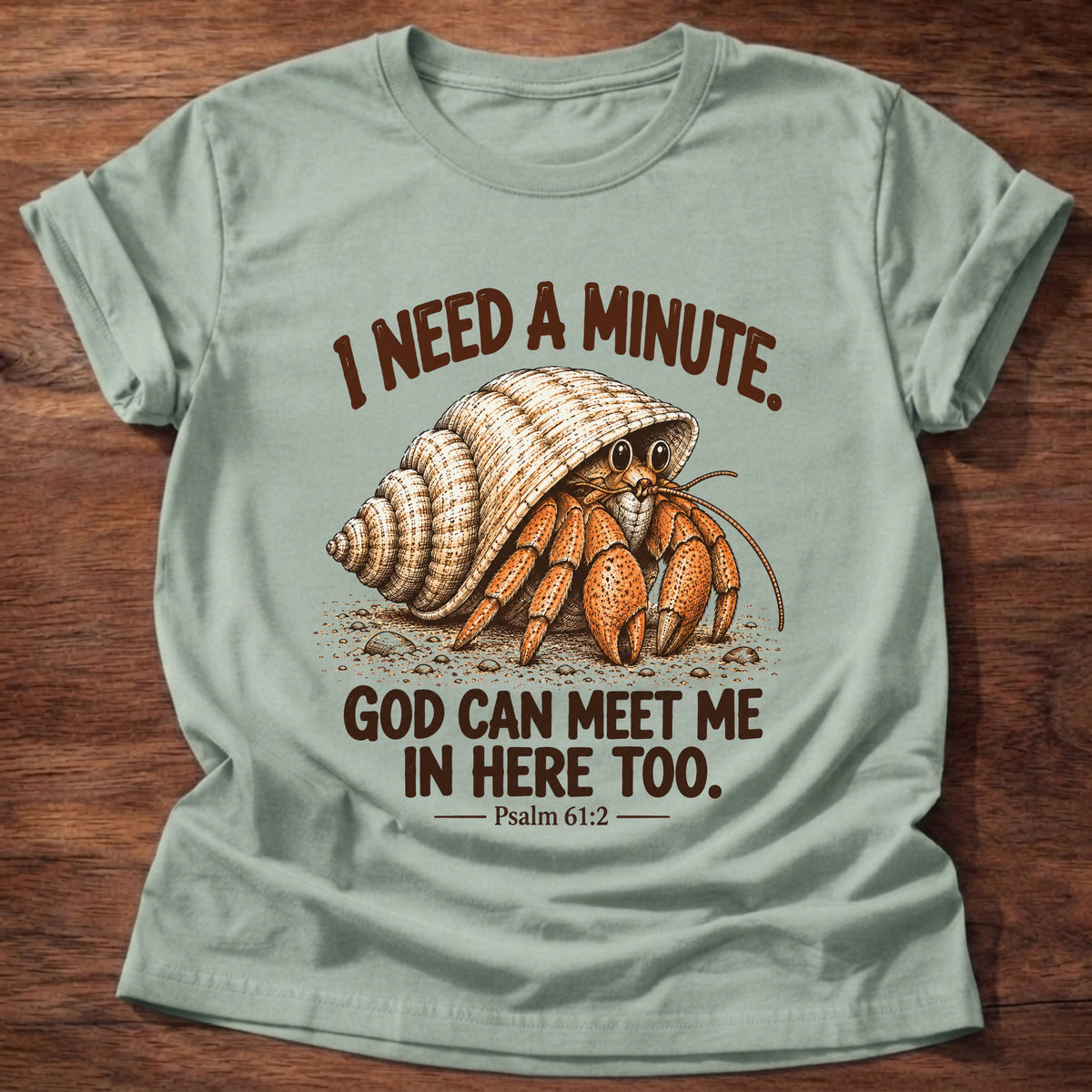 Sage t-shirt printed with a hermit crab peeking out of its spiral shell graphic and “I need a minute. God can meet me in here too.” Psalm 61:2 faith based gift