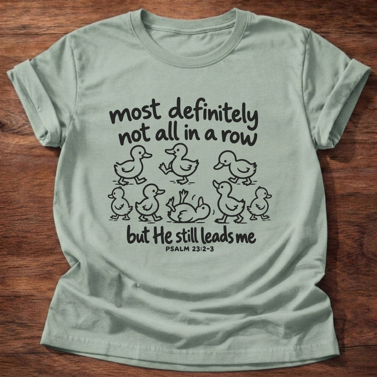 Sage t-shirt printed with a scattered line of hand-drawn ducklings graphic and “Most definitely not all in a row, but He still leads me.” Psalm 23:2-3 Christian shirt