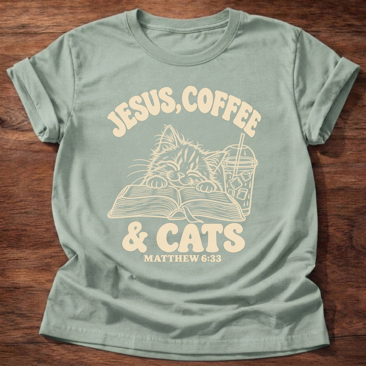 Sage t-shirt printed with a kitten reading an open Bible beside an iced coffee and “Jesus, Coffee & Cats” Matthew 6:33 Christian shirt