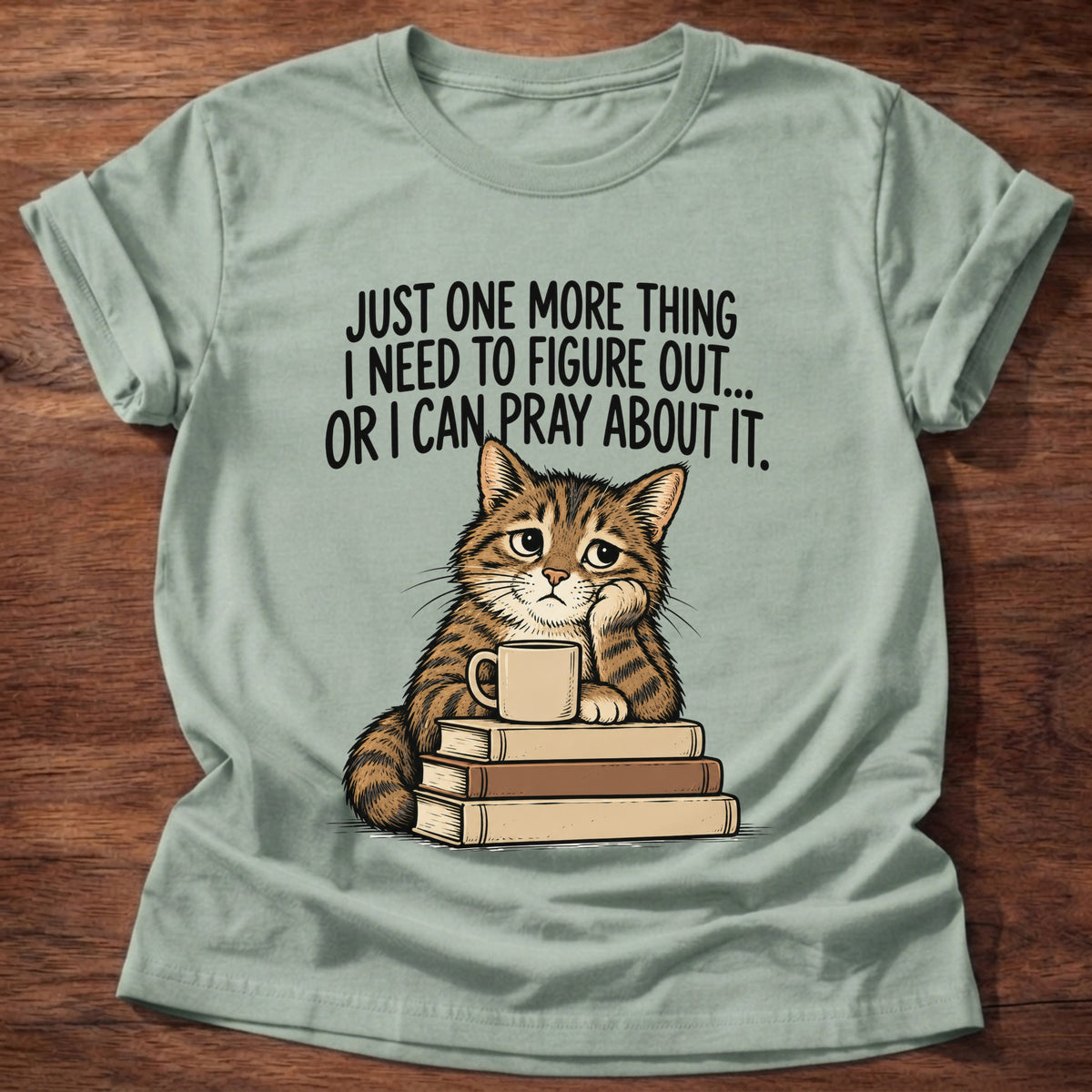 Sage t-shirt printed with a cat surrounded by books graphic and 'Just one more thing I need to figure out... or I can pray about it.' Philippians 4:6-7 faith based gift