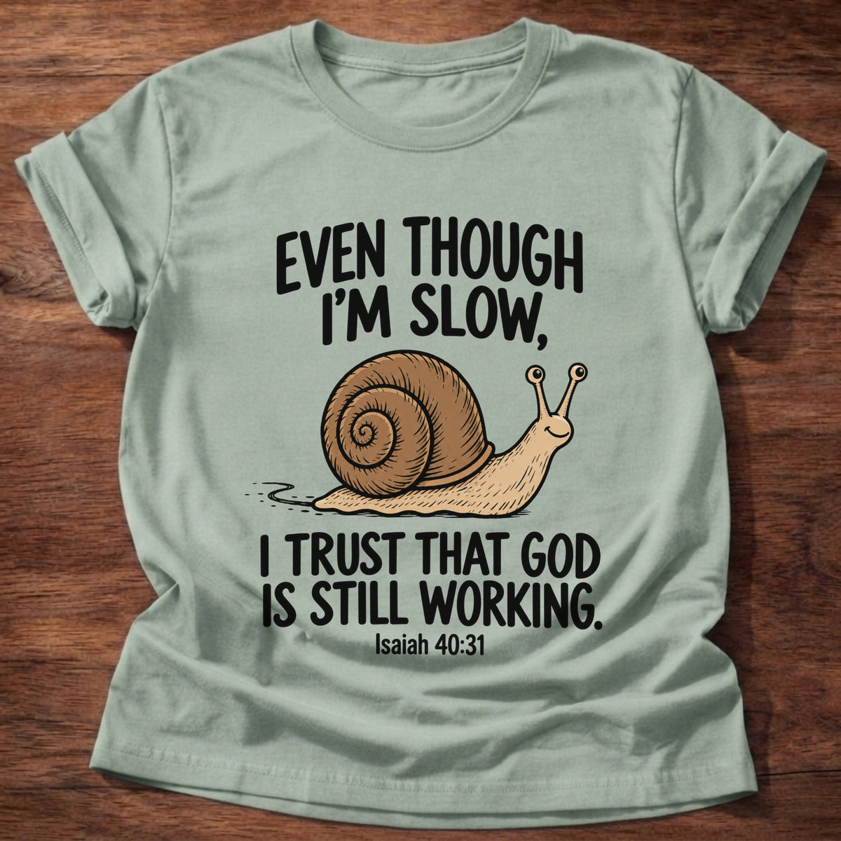 Sage t-shirt printed with a snail graphic and 'Even though I'm slow. I trust that God is still working.' Isaiah 40:31 faith based gift