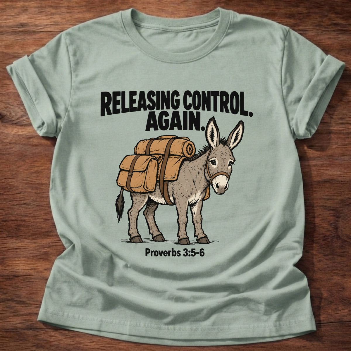 Sage t-shirt printed with a donkey carrying a backpack graphic and 'Releasing control. Again.' Proverbs 3:5-6 faith based gift