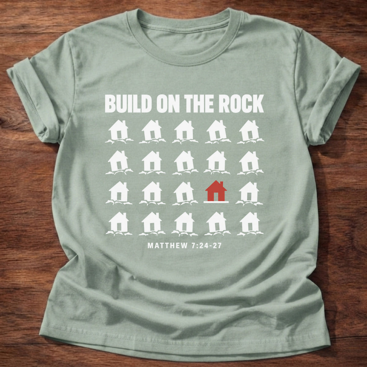 Sage t-shirt printed with a row of houses graphic and 'Build on the rock.' Matthew 7:24-27 faith based gift
