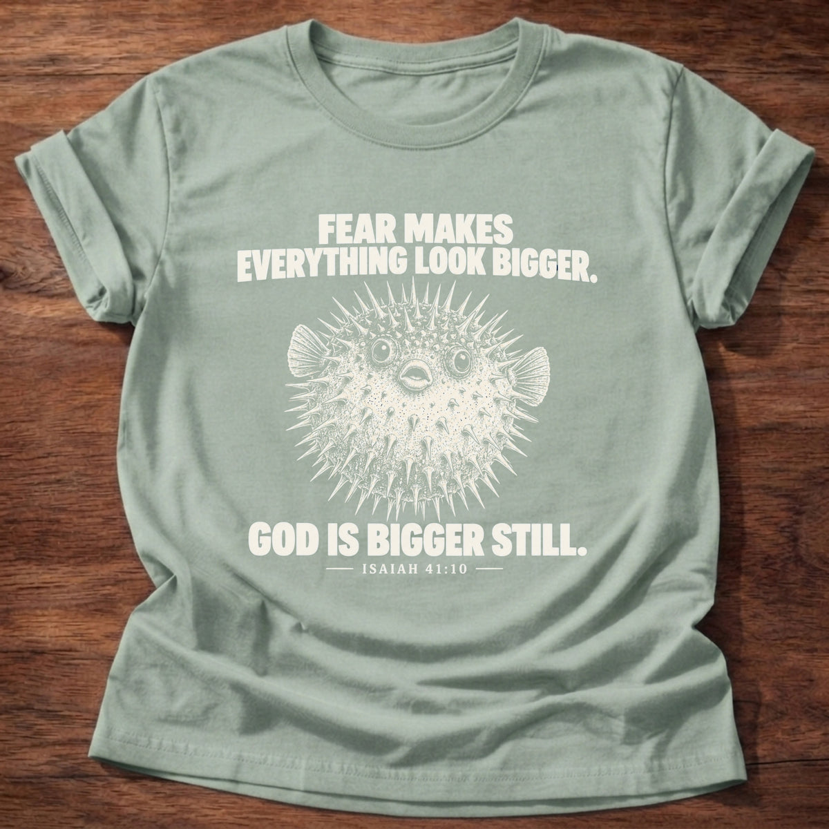 Sage t-shirt printed with a pufferfish inflated to look bigger graphic and 'Fear makes everything look bigger. God is bigger still.' Isaiah 41:10 faith based gift