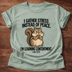 Sage t-shirt printed with a squirrel gathering acorns graphic and 'I gather stress instead of peace. I'm learning contentment.' Luke 12:15 faith based gift